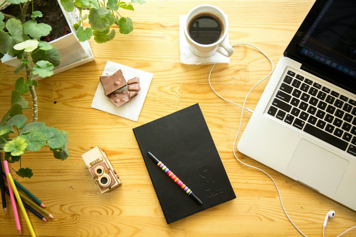Laptop, notebook, and coffee arranged on a wooden desk.
