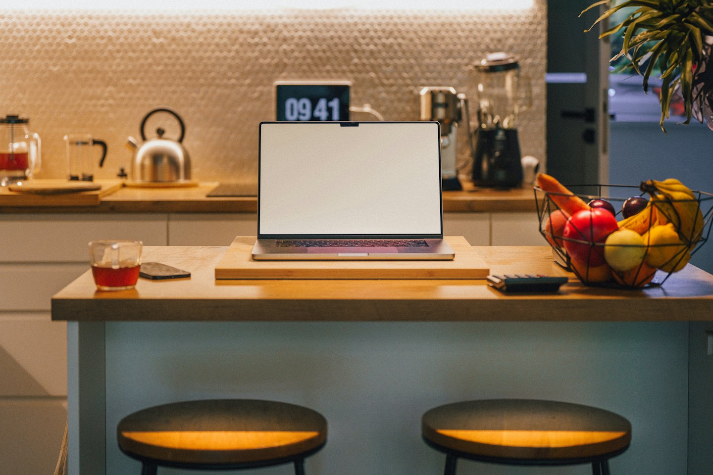 Laptop on kitchen island with fruit and drink.